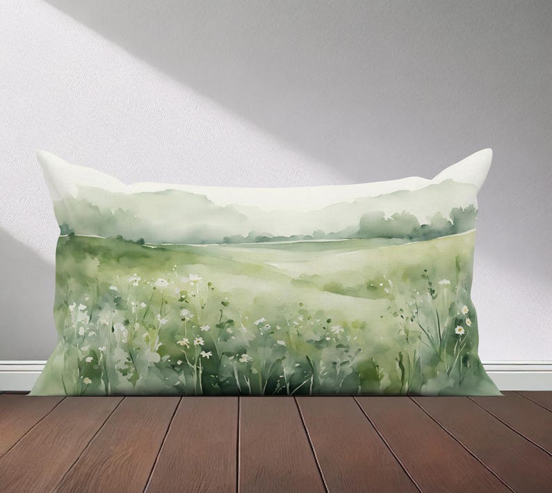 Peut inclure: Un oreiller en aquarelle vert et blanc repr&eacute;sentant une sc&egrave;ne de paysage avec un champ de fleurs et une cha&icirc;ne de montagnes au loin.