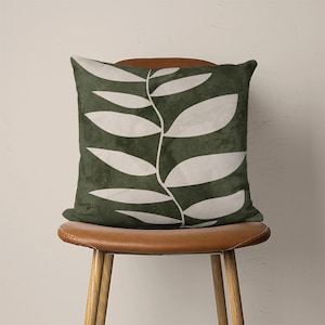 May include: A green throw pillow with a white leaf design. The pillow is sitting on a brown leather chair.