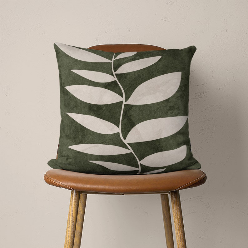 May include: A green throw pillow with a white leaf design. The pillow is sitting on a brown leather chair.