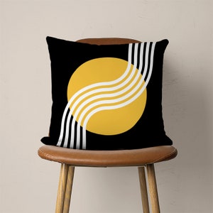 May include: Black and yellow throw pillow with a geometric design. The pillow features a large yellow circle with white curved lines and a black background.