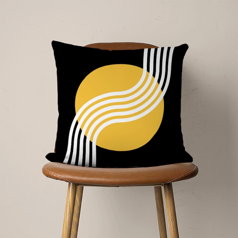 May include: Black and yellow throw pillow with a geometric design. The pillow features a large yellow circle with white curved lines and a black background.