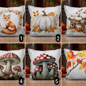 Pode incluir: Almofadas decorativas quadradas com designs de outono. As almofadas apresentam uma raposa em uma coroa de flores, uma abóbora branca com rosas, abóboras em um carrinho, cogumelos e folhas de outono. As almofadas têm um fundo branco.