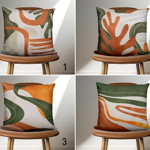 Op de afbeelding: Vier kussens met abstracte ontwerpen in tinten groen, oranje en bruin. De kussens liggen op stoelen met bruine leren zittingen.