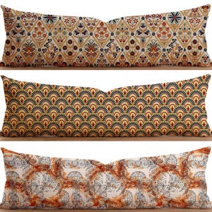 May include: Three long decorative throw pillows with different patterns. The first pillow has a geometric pattern with red, yellow, and blue colors. The second pillow has a pattern of yellow and blue semicircles. The third pillow has a white background with a brown and orange pattern.