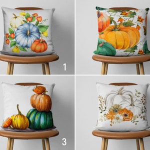 May include: Four different pillow designs featuring watercolor illustrations of pumpkins and fall foliage. The pillows are white with a brown leather backing and are displayed on brown wooden chairs.