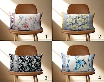 May include: Four decorative throw pillows with floral patterns. The pillows are on brown chairs with wooden legs. The pillows have a white background with blue, yellow, pink, and black floral designs. The pillows have a blue and white geometric border.