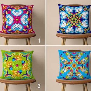 May include: Four decorative throw pillows with colourful geometric patterns. The pillows are displayed on chairs with brown wooden frames.