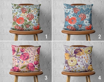 May include: Four different floral patterned throw pillows displayed on brown chairs with a white brick background. Each pillow features a different color scheme and floral design.