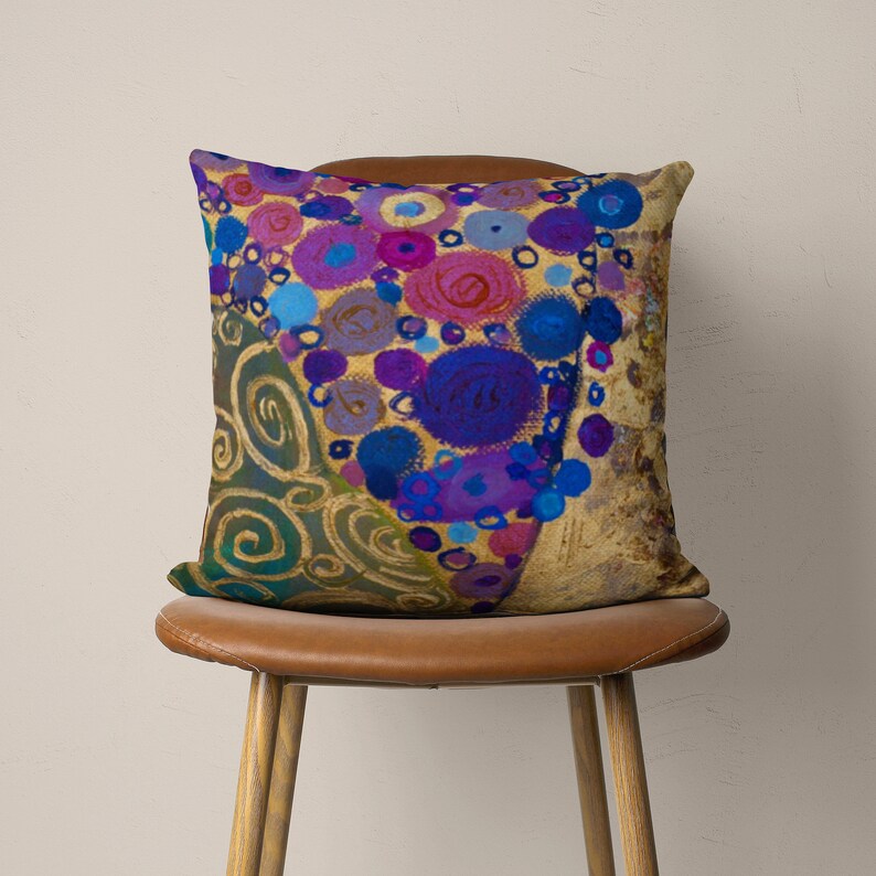 Puede incluir: Una almohada de tiro colorida con un patr&oacute;n de c&iacute;rculos azules, morados y rosados sobre un fondo dorado. La almohada est&aacute; sentada en una silla de cuero marr&oacute;n.