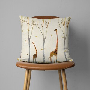 May include: A throw pillow with a cream background and a pattern of brown giraffes and trees. The giraffes are silhouetted against a white background and have a textured, marbled appearance.