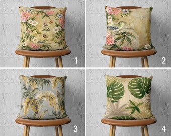 May include: Four decorative throw pillows with floral and botanical designs. Pillows feature various patterns including pink flowers, birds, and tropical leaves. Each pillow is square and rests on a brown wooden stool against a white brick wall.