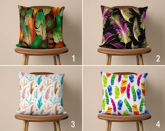 May include: Four different pillow covers with feather patterns. The first pillow cover has a green, brown, and orange feather pattern. The second pillow cover has a black background with gold and purple feathers. The third pillow cover has a white background with watercolor-style green, orange, and pink feathers. The fourth pillow cover has a white background with colorful feathers.
