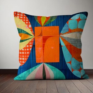 Op de afbeelding: Een kleurrijk kussen met een geometrisch ontwerp met een groot oranje vierkant in het midden, omringd door blauwe, groene, gele en rode vormen.