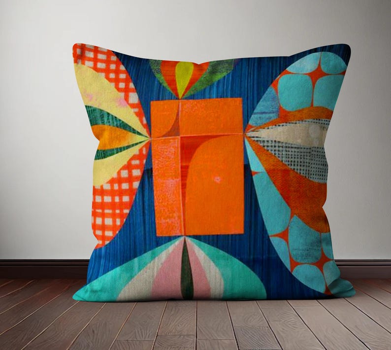 Op de afbeelding: Een kleurrijk kussen met een geometrisch ontwerp met een groot oranje vierkant in het midden, omringd door blauwe, groene, gele en rode vormen.