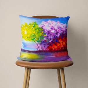 May include: A colorful throw pillow with a painting of trees reflected in a lake. The trees are painted in shades of yellow, purple, and red.