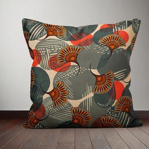 Op de afbeelding: Een decoratief kussen met een geometrisch patroon met abstracte vormen in grijstinten, oranje en rood. Het patroon bevat gestileerde waaiers en cirkels.