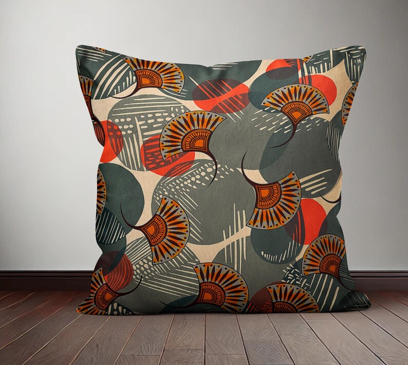 Op de afbeelding: Een decoratief kussen met een geometrisch patroon met abstracte vormen in grijstinten, oranje en rood. Het patroon bevat gestileerde waaiers en cirkels.