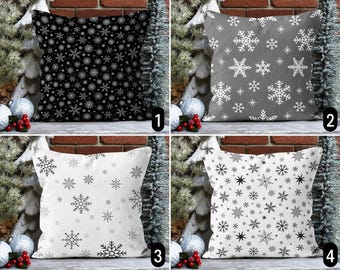 Puede incluir: Cuatro almohadas decorativas con patrones de copos de nieve. Las almohadas son en blanco y negro, gris y blanco, y blanco con copos de nieve negros. Las almohadas están dispuestas en una fila sobre un fondo de pared de ladrillo.