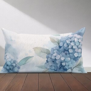 Peut inclure: Un oreiller en tissu doux et textur&eacute; avec un motif aquarelle de fleurs d'hortensias bleues et de feuilles vertes. L'oreiller pr&eacute;sente un effet aquarelle subtil.