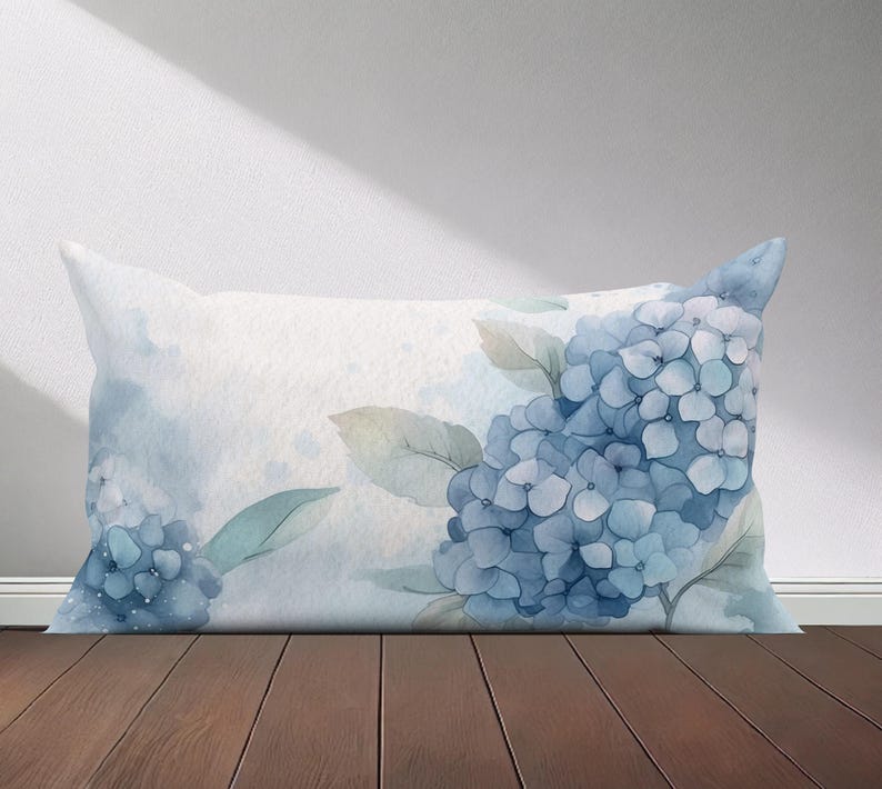 Peut inclure: Un oreiller en tissu doux et textur&eacute; avec un motif aquarelle de fleurs d'hortensias bleues et de feuilles vertes. L'oreiller pr&eacute;sente un effet aquarelle subtil.