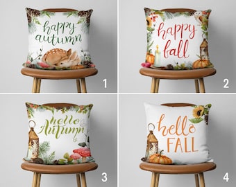 Op de afbeelding: Vier decoratieve sierkussens met herfstthema's. Elk kussen heeft een witte achtergrond met herfstafbeeldingen, waaronder pompoenen, bladeren en bosdieren. De kussens hebben tekst met de tekst "happy autumn", "happy fall", "hello autumn" en "hello fall".