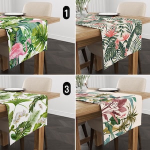 May include: Four different table runners featuring tropical leaf designs. The runners are displayed on wooden tables with chairs. The patterns include pink flamingos, red flowers, white orchids, and pink and green leaves.