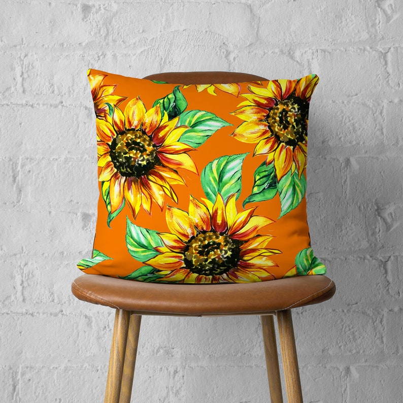 May include: Orange throw pillow with a sunflower pattern. The pillow features a repeating pattern of yellow sunflowers with green leaves on an orange background.
