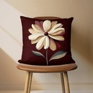 May include: A burgundy throw pillow with a large, stylized white and beige flower design.