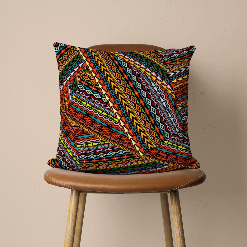 Op de afbeelding: Een kleurrijk kussen met een geometrisch patroon in tinten oranje, rood, geel, blauw, groen en zwart. Het kussen ligt op een bruine leren stoel.
