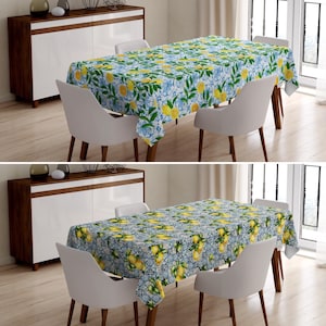 May include: Two dining tables with white chairs and a lemon and blue floral tablecloth. The tablecloth has a repeating pattern of lemons and blue flowers on a white background.