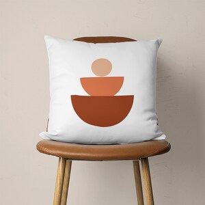 Pu&ograve; includere: Cuscino bianco con un design geometrico di tre semicerchi impilati in tonalit&agrave; arancio e marrone.