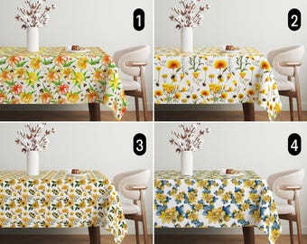 May include: Four different tablecloths with floral patterns. The tablecloths are white with yellow, orange, and blue flowers. The tablecloths are shown on a table with a white background.