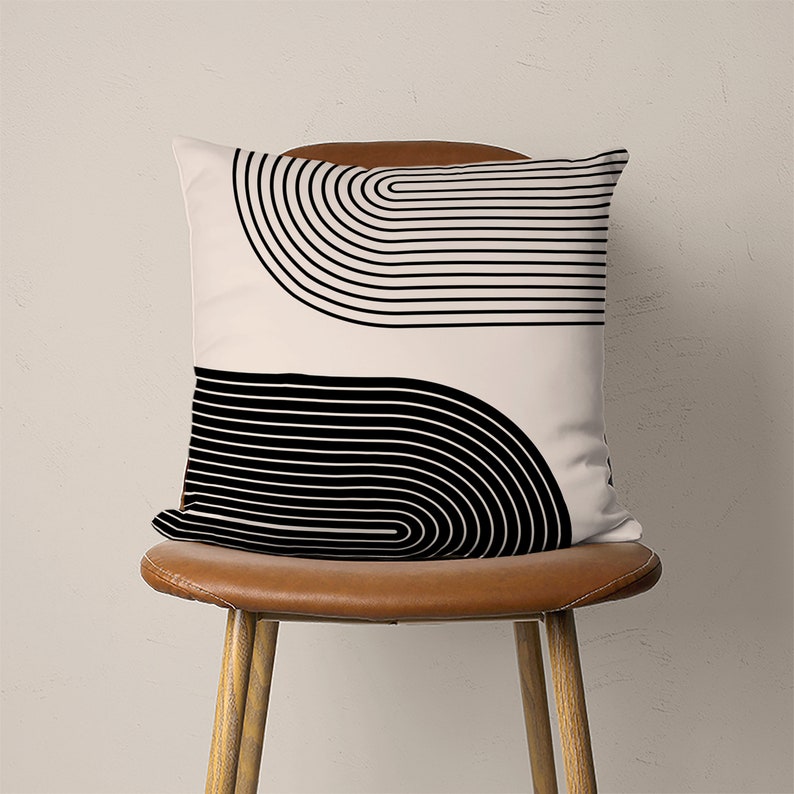 May include: A white throw pillow with a black and white geometric design of overlapping curved lines. The pillow is sitting on a brown leather chair.