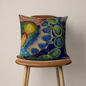 May include: A colourful throw pillow with a blue, green, yellow, and pink abstract pattern. The pillow has a unique design with swirling shapes and circles.