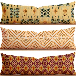Puede incluir: Tres almohadas largas decorativas con patrones geométricos. La primera almohada tiene un fondo amarillo con formas geométricas azules y naranjas. La segunda almohada tiene un fondo blanco con formas geométricas naranjas. La tercera almohada tiene un fondo burdeos con formas geométricas naranjas y amarillas.
