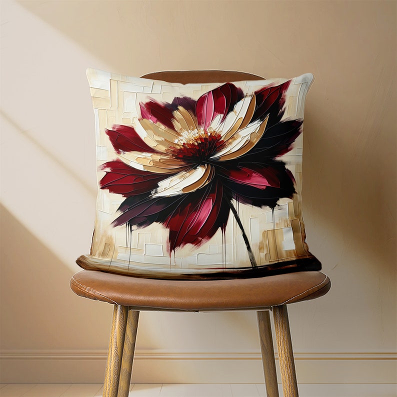 May include: A decorative throw pillow with a large, abstract floral design in shades of burgundy, white, and gold. The pillow is sitting on a brown leather chair.