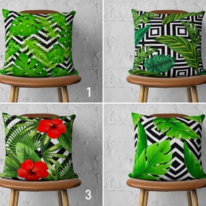 Può includere: Quattro cuscini decorativi con disegni di foglie e fiori tropicali. Ogni cuscino presenta un motivo diverso di foglie verdi e fiori di ibisco rossi su uno sfondo geometrico bianco e nero. I cuscini sono esposti su sgabelli di legno marroni.
