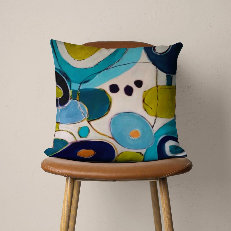 May include: A decorative throw pillow with an abstract design featuring blue, green, and white circles and swirls on a white background.