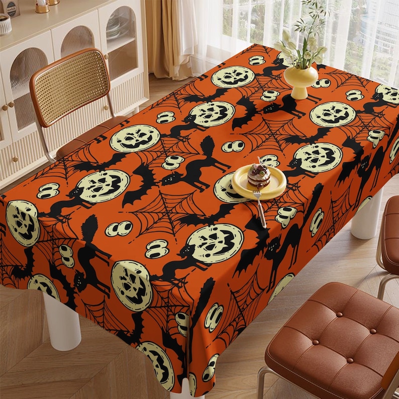 May include: Orange tablecloth with a Halloween theme featuring black bats, spiderwebs, and jack-o'-lantern faces.