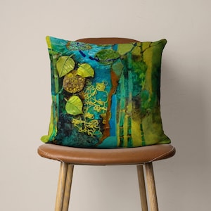 May include: A decorative cushion with an abstract design featuring green, blue and yellow colours. The cushion has a textured surface and a unique, artistic pattern.