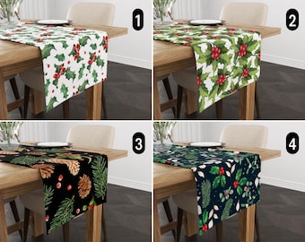 Könnte beinhalten: Vier verschiedene Tischläufer mit festlichen Designs. Der erste Tischläufer hat einen weißen Hintergrund mit grünen Stechpalmenblättern und roten Beeren. Der zweite Tischläufer hat einen grünen Hintergrund mit weißen Stechpalmenblättern und roten Beeren. Der dritte Tischläufer hat einen schwarzen Hintergrund mit grünen Kiefernästen, Zapfen und roten Beeren. Der vierte Tischläufer hat einen dunkelblauen Hintergrund mit grünen Stechpalmenblättern und roten Beeren.