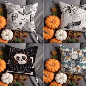 May include: Four decorative throw pillows with Halloween themes. The pillows are white with black and gray skulls, bats, and spiderwebs. Another pillow is black with white text that says "Let's Get Spooky" and a cartoon skull. The last pillow is white with a floral pattern and black skulls.