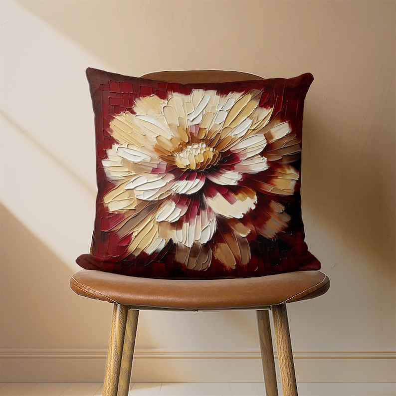 May include: A red and cream throw pillow with a large, abstract floral design. The pillow is sitting on a brown leather chair.