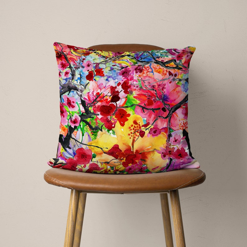 May include: A colorful throw pillow with a watercolor floral design featuring pink, red, yellow, and blue flowers. The pillow is on a brown chair.