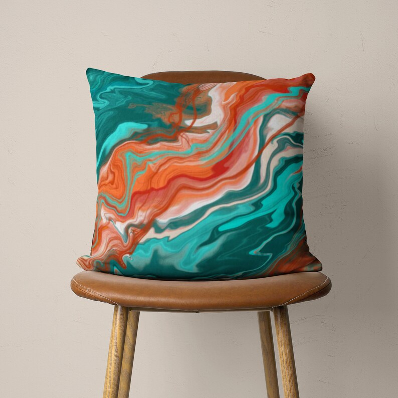 May include: Teal and orange abstract throw pillow with a marbled design. The pillow is sitting on a brown chair.