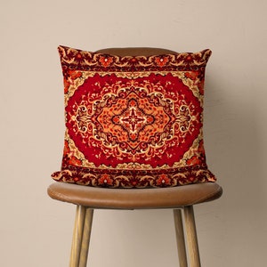 May include: A red throw pillow with a gold and orange patterned design. The pattern is reminiscent of a traditional Persian rug.
