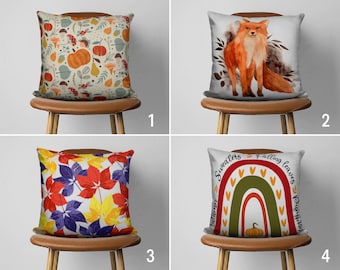 Può includere: Quattro cuscini decorativi con disegni a tema autunnale. Uno presenta zucche, funghi e fogliame. Un altro mostra una volpe ad acquerello. Il terzo mostra foglie colorate e l'ultimo ha un arcobaleno e il testo "Sweaters, falling leaves, pumpkin."