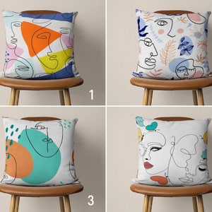 May include: Four throw pillows with different abstract line art designs. The pillows are white with colorful accents. The designs feature faces, butterflies, and geometric shapes.
