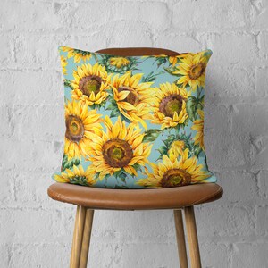 May include: A blue throw pillow with a watercolor pattern of sunflowers. The pillow is sitting on a brown chair.
