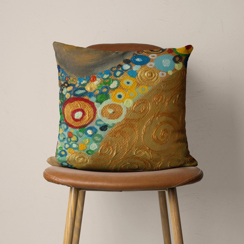 Puede incluir: Una almohada decorativa con un dise&ntilde;o abstracto colorido que presenta c&iacute;rculos, remolinos y puntos en tonos de amarillo, azul, verde, rojo y dorado. La almohada est&aacute; sentada en una silla de cuero marr&oacute;n.